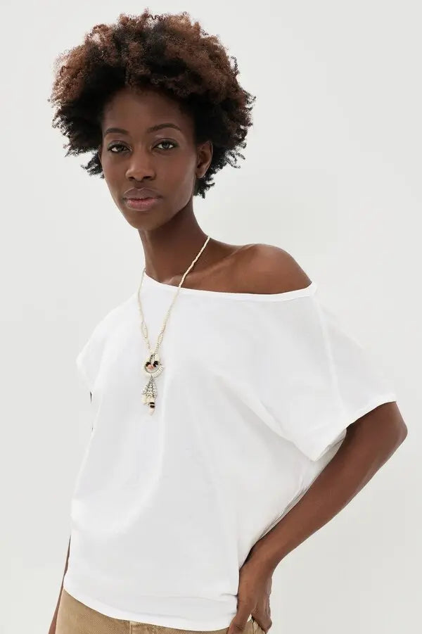 Woman wearing a white off-shoulder top and beige pants against a plain background