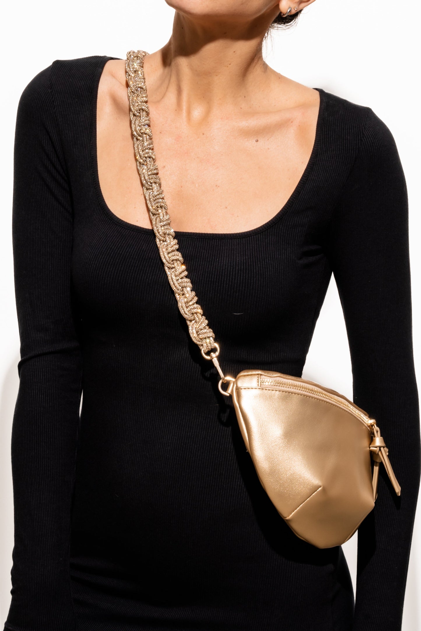 Person wearing a black top with a gold handbag over their shoulder on a white background