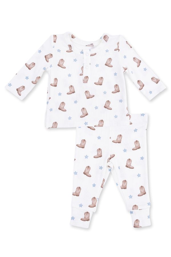 A two-piece baby pajama set featuring a long-sleeve top and matching pants in white, decorated with a repeating pattern of mini brown cowboy boots and light blue stars.
