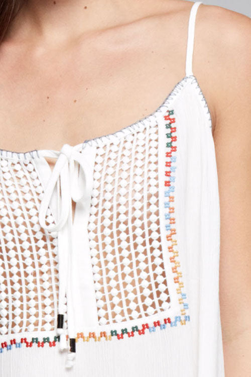 Close-up of a white embroidered crochet camisole top with thin straps, a front tie closure, and multicolored embroidered border details.