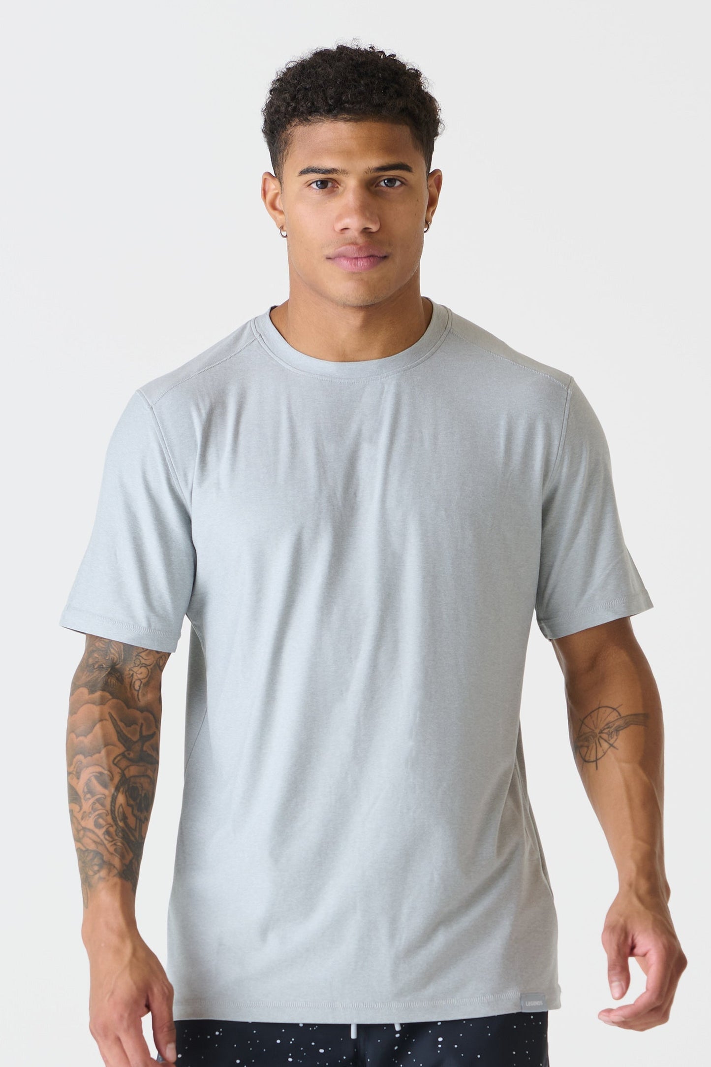 A man wearing a heather gray crew-neck t-shirt, standing against a solid light gray background.
