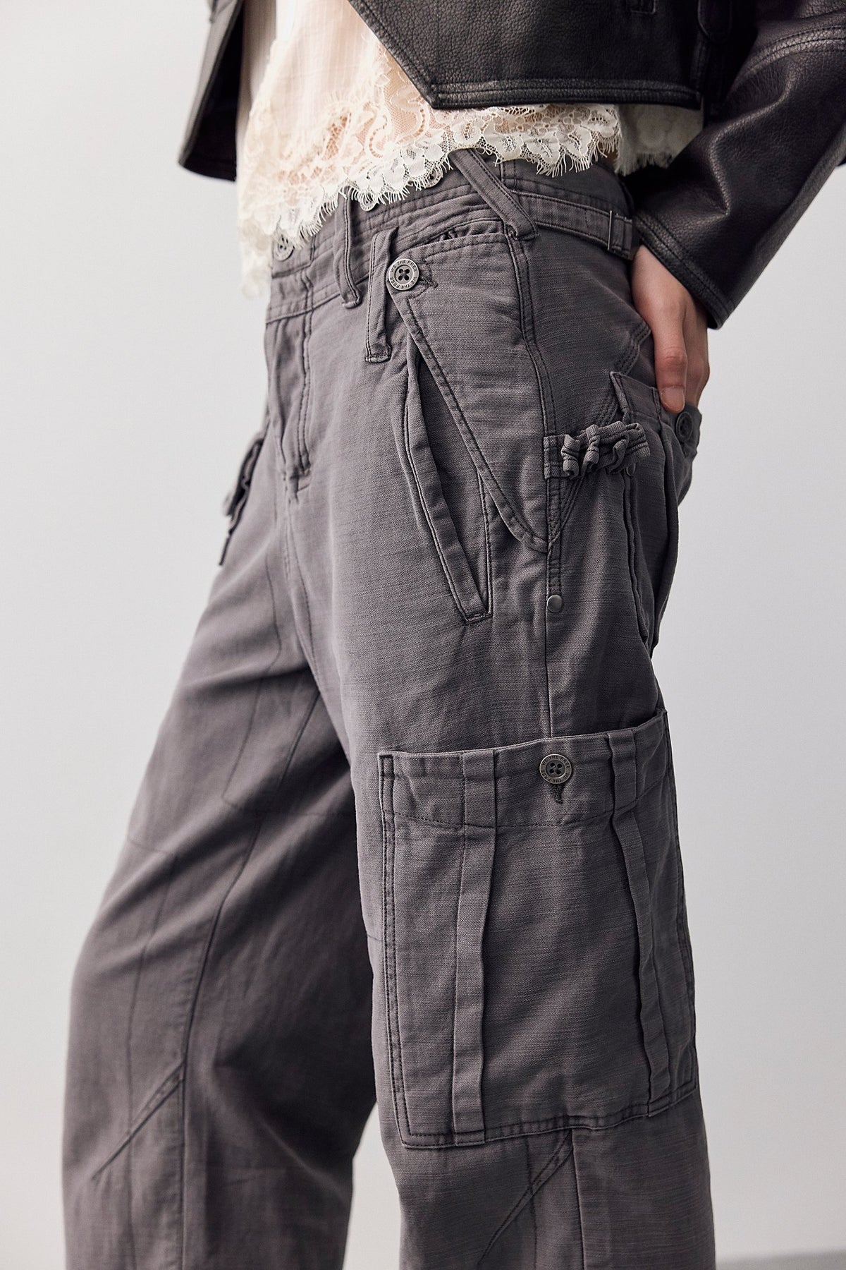 Side view of woman wearing a cream lace top, black leather jacket and Tight Fuse Slim Utility Pant in Charcoal Grey