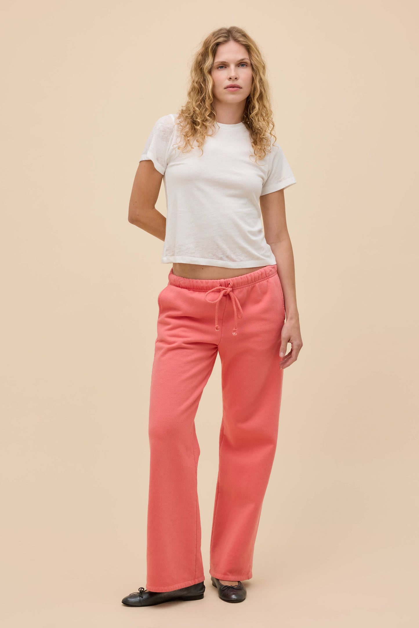 Woman wearing a white burnout vintage t-shirt and pink pants on a beige background