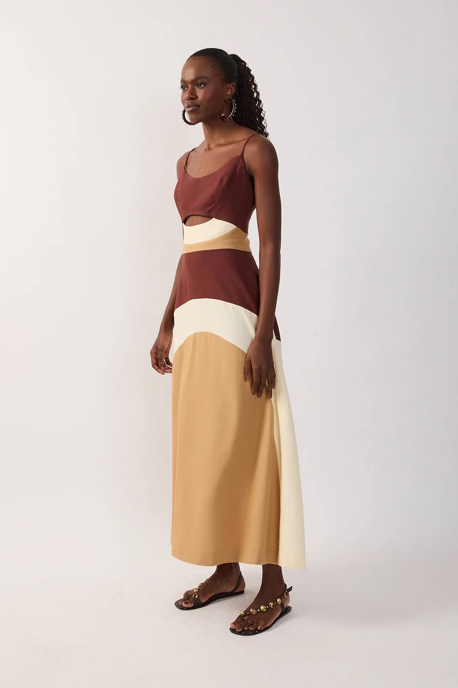 Side view of woman wearing a multicolor-blocked dress with brown, white, and beige sections & a cutout on a white background