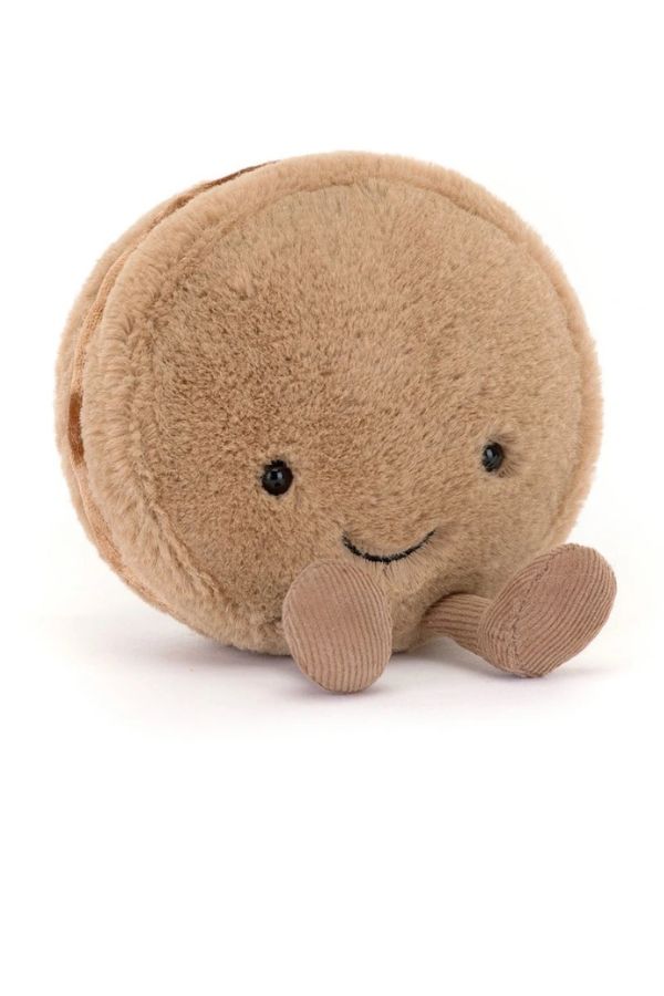 A round, soft plush toy shaped like a smiling macaron called "Mona Macaron" in a warm chocolate color, with small black eyes and a stitched smile, photographed on a clean white background.