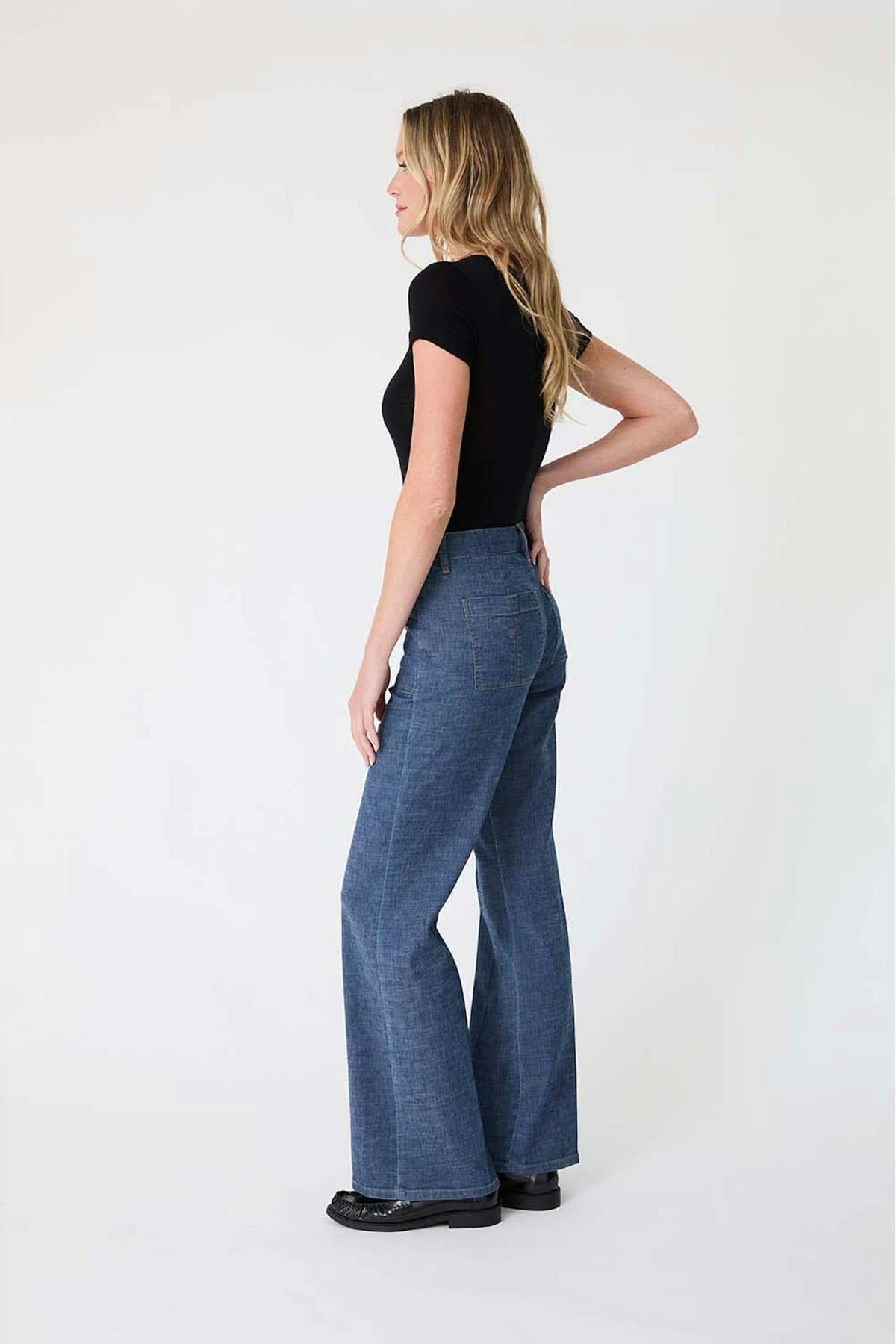 A woman shown from the side wearing a black short-sleeve top and high-waisted, Sarah pants in Stargazer color against a plain white studio background.