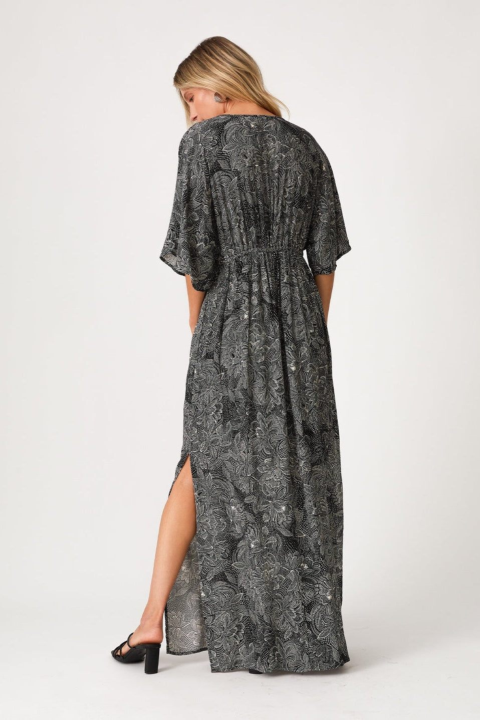 Woman wearing a black and natural patterned dress with a slit on a white background