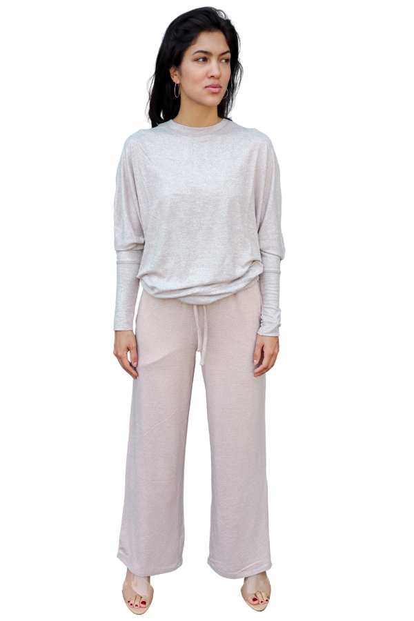 Woman wearing a light pink long-sleeve top and beige wide-leg pants on a white background