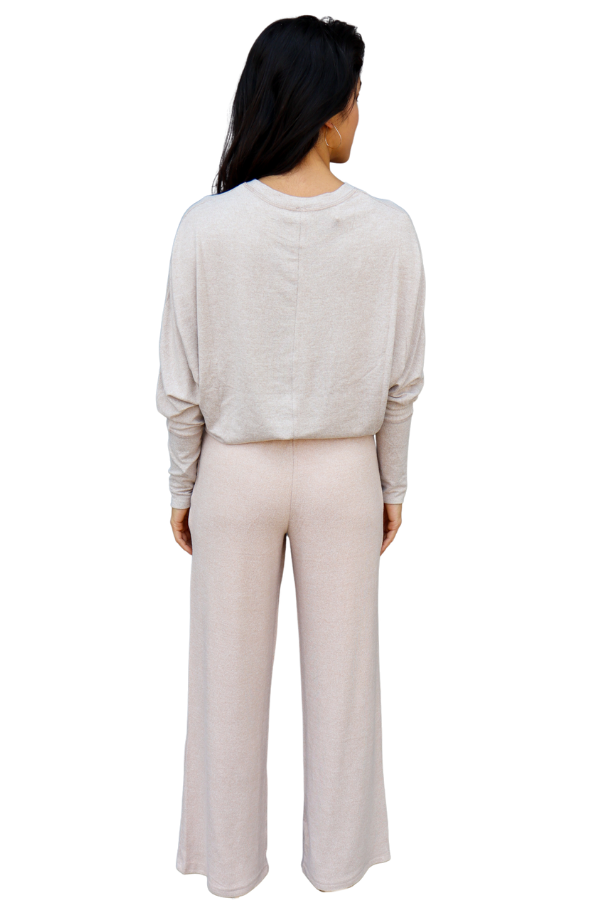 Woman wearing a light pink long-sleeve top and beige wide-leg pants on a white background