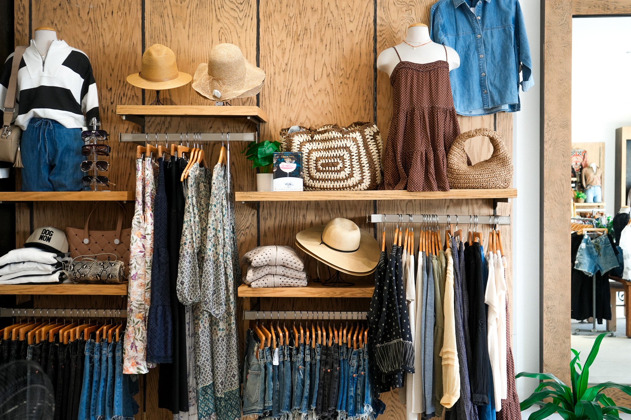 Clothing store display with racks of clothes, hats, and bags on wooden shelves.