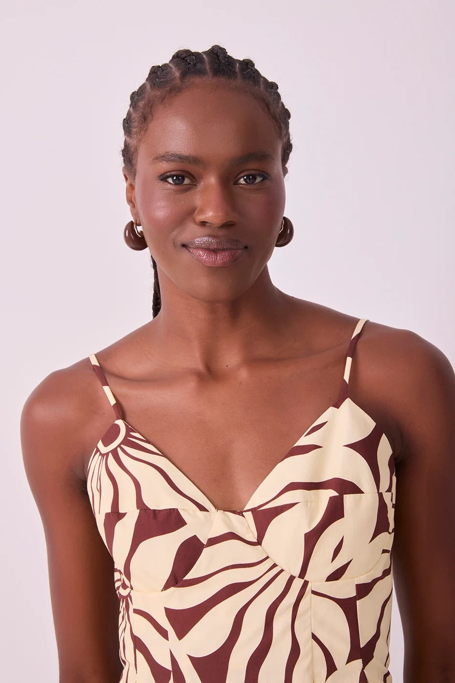 A woman with braided hair wearing a beige and dark brown abstract alvorecer patterned camisole top, photographed against a plain light background.