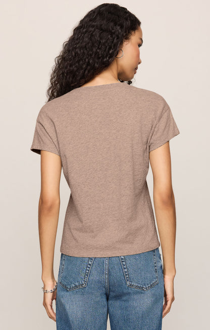 A woman shown from the back wearing a short-sleeve crewneck t-shirt in a heathered ash color, paired with blue jeans, against a solid light beige background.
