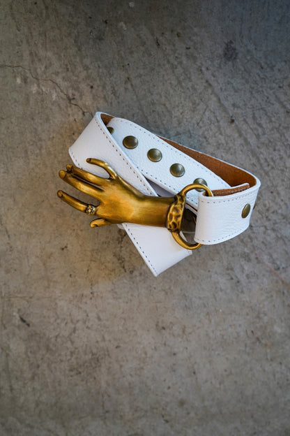 White leather belt with gold hand charm on a textured surface