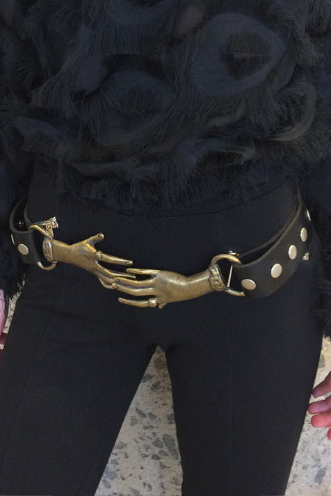 Person wearing a black outfit with a unique belt featuring a hand design.