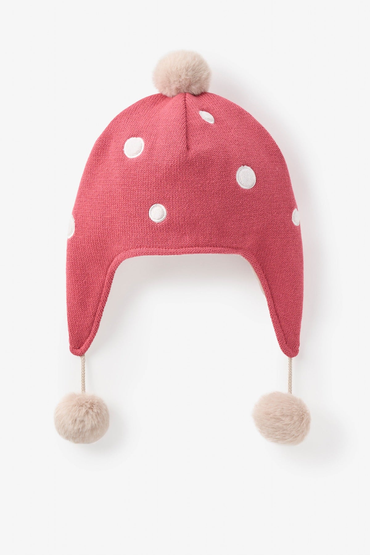 Red mushroom knit baby hat with white polka dots and pom-poms on a light beige background