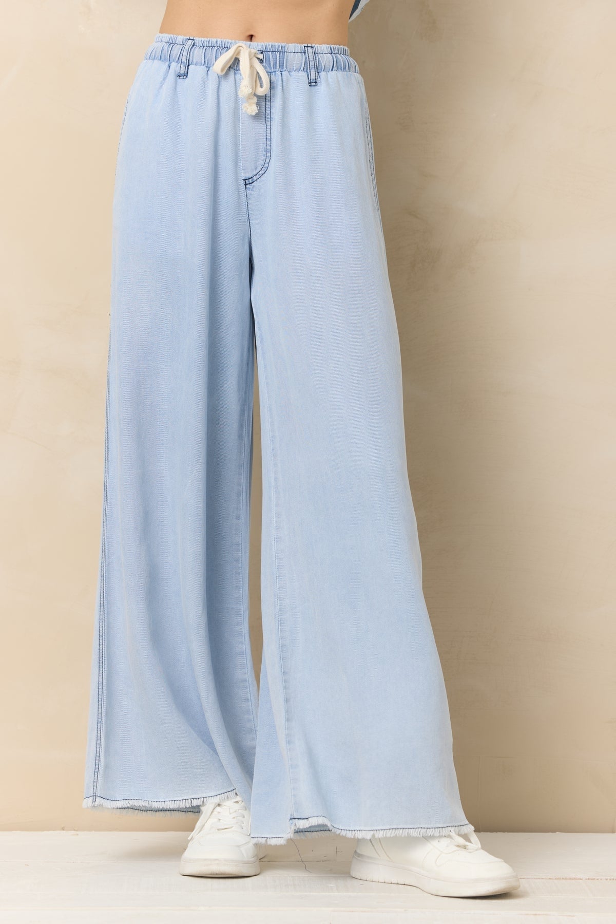 Light wash denim wide-leg pants with elastic waist, drawstring, and front seam detailing