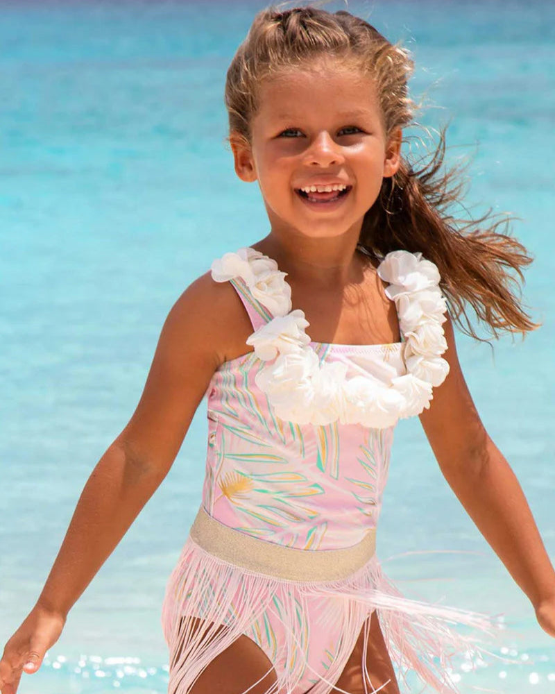 Young girl in a colorful swimsuit with floral details on a beach.