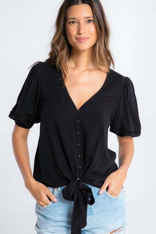 Woman wearing a black tie-front blouse and light blue jeans on a white background