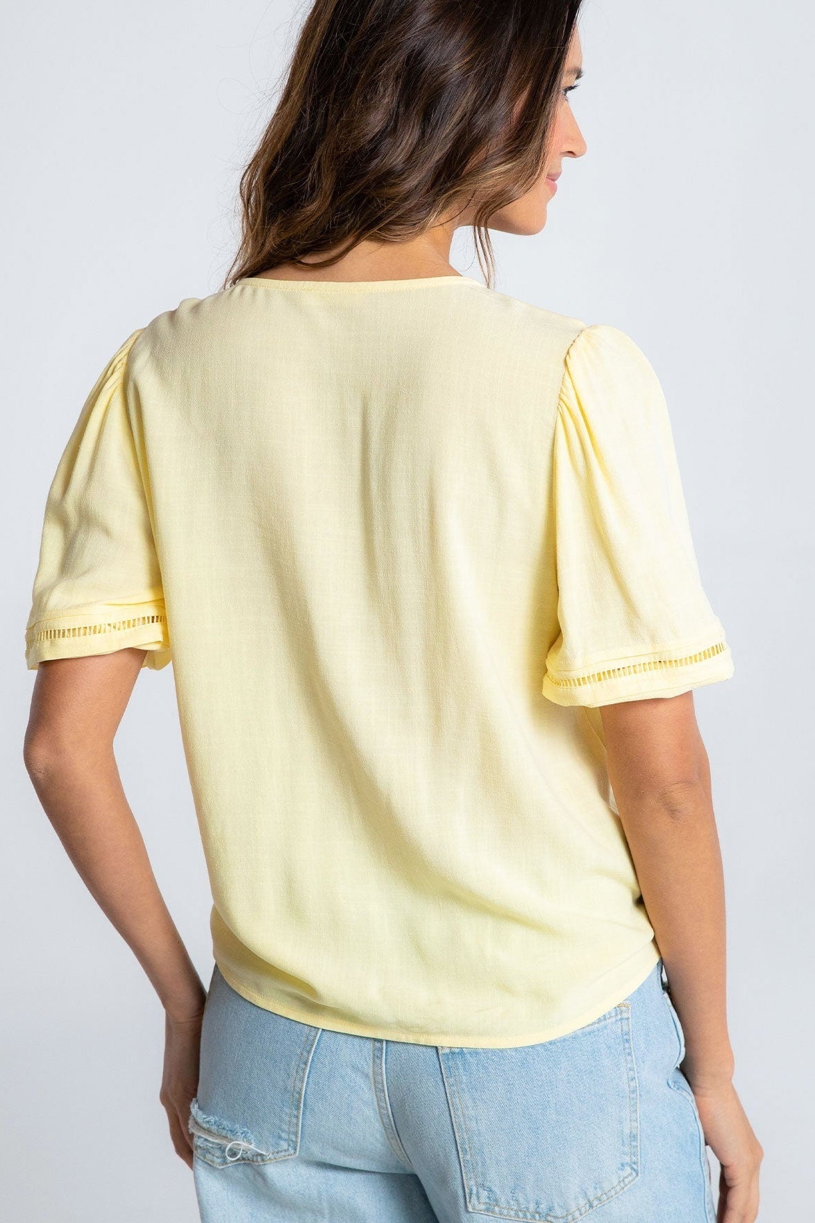 Woman wearing a light yellow top with ruffled sleeves against a plain background