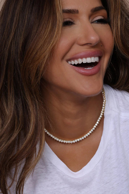 Gold tennis necklace with white crystal pavé, worn close-up on neckline