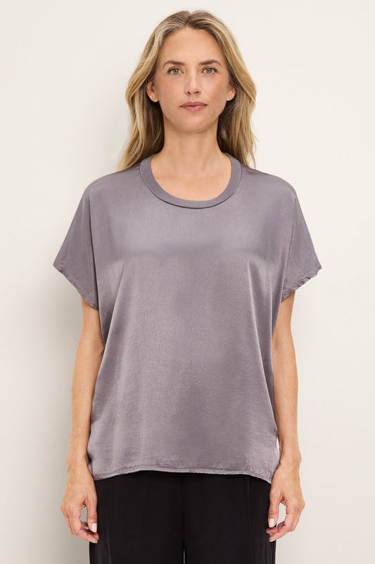 A woman modeling a short-sleeve crewneck top in a thunder gray color, paired with black pants, against a plain off-white background.