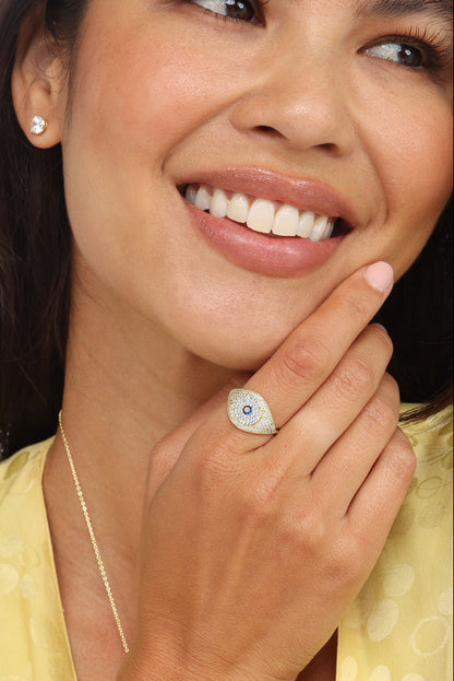 Gold evil eye ring with blue center and pavé stones, worn on finger
