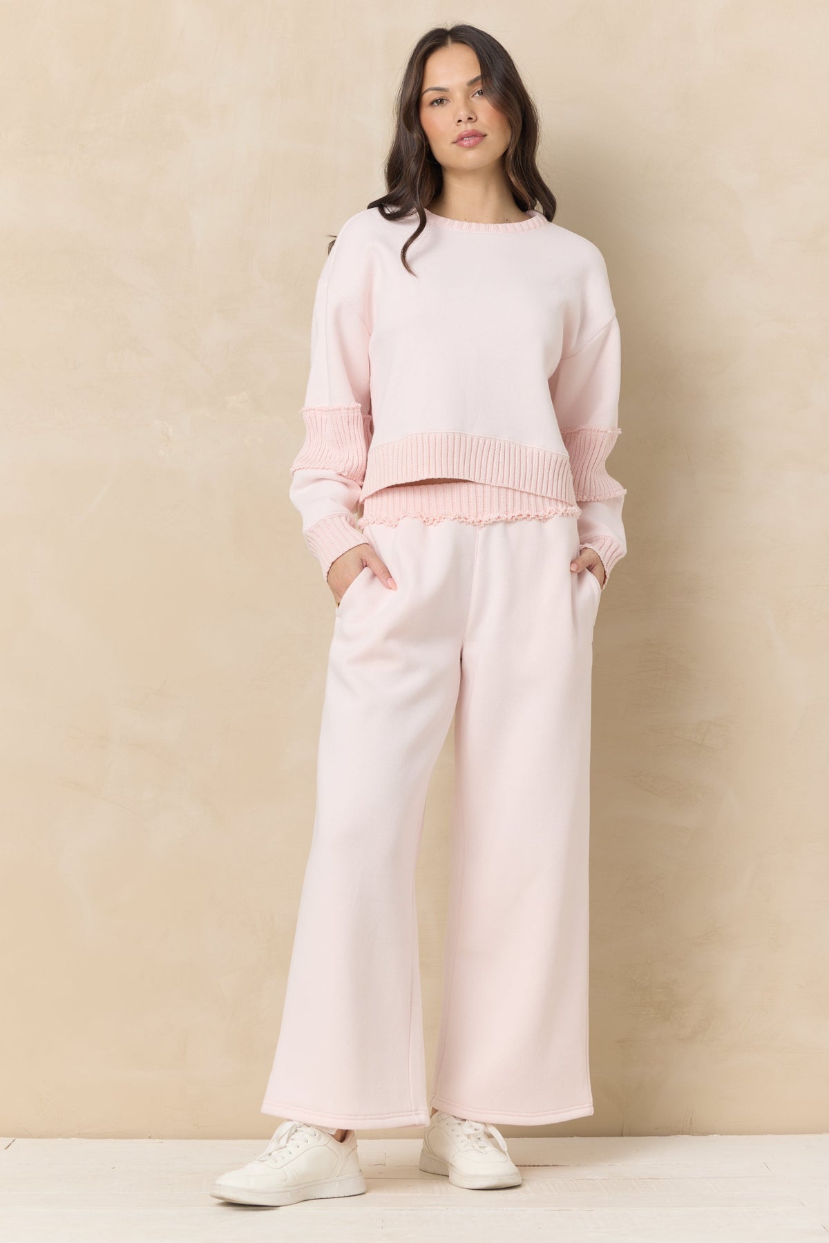 Woman wearing a hibiscus pink sweater and matching rib fleece pants against a beige background