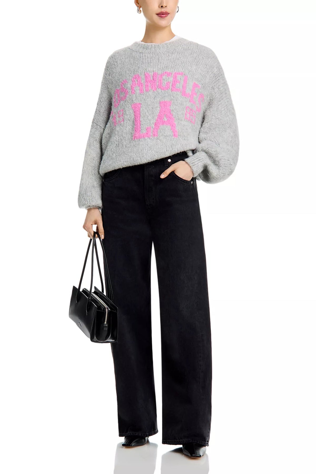 A model wearing a light gray fuzzy knit sweater with a pink 'Los Angeles LA' graphic, paired with black wide-leg jeans and holding a small black handbag against a plain white background.