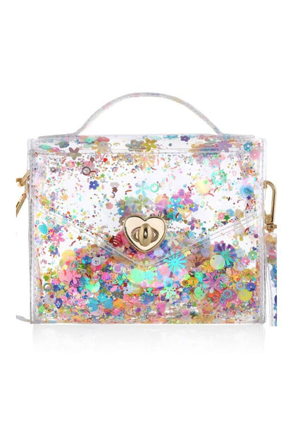 A clear plastic handbag filled with multicolored flower-shaped glitter, featuring a gold heart-shaped clasp, a top handle, and a matching wristlet strap on a white background.