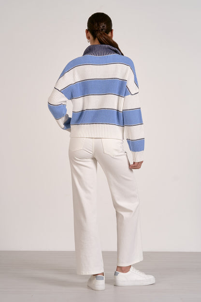 Back view of person wearing a light blue and white striped sweater with white pants on a plain background