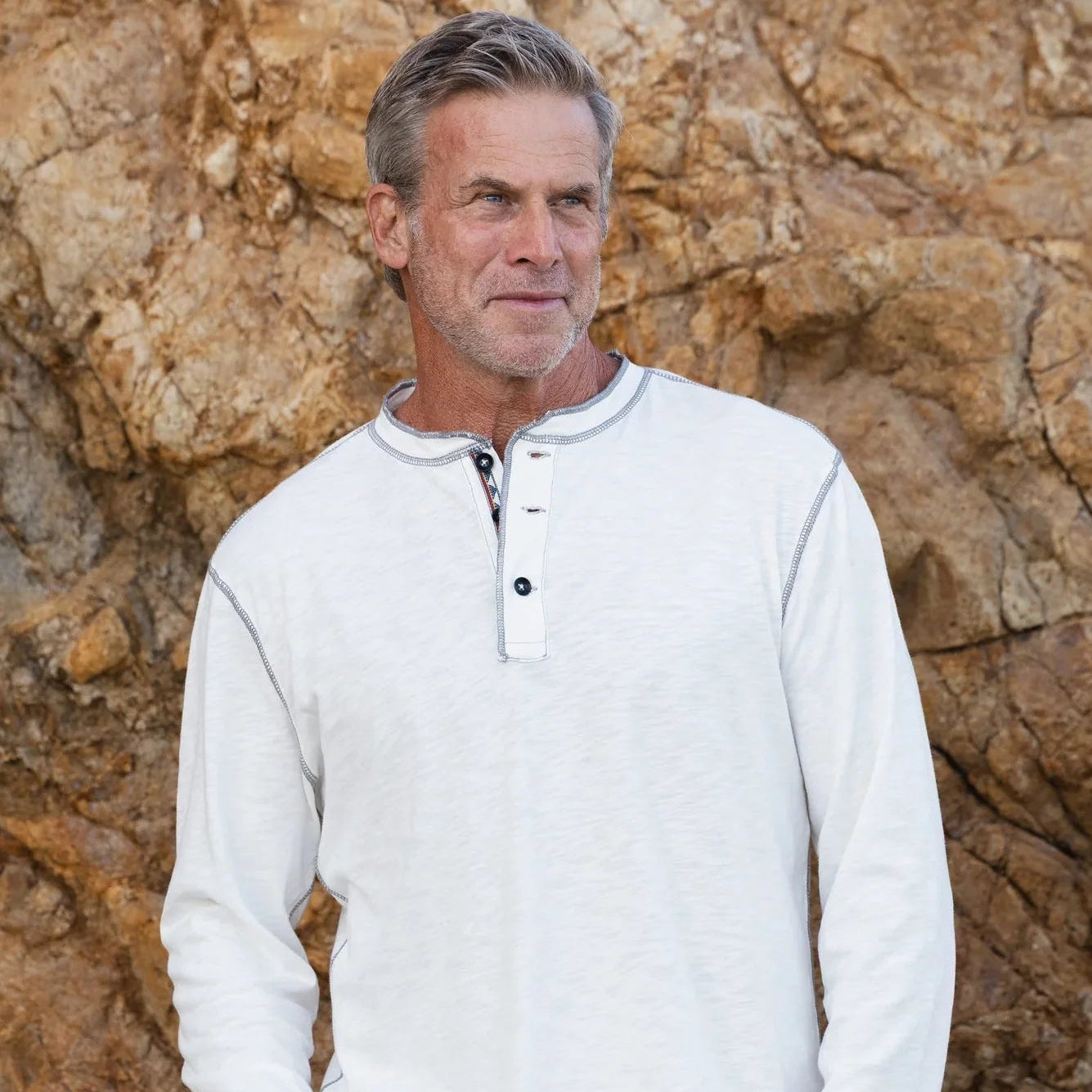 Man wearing a white long-sleeve shirt against a stone wall