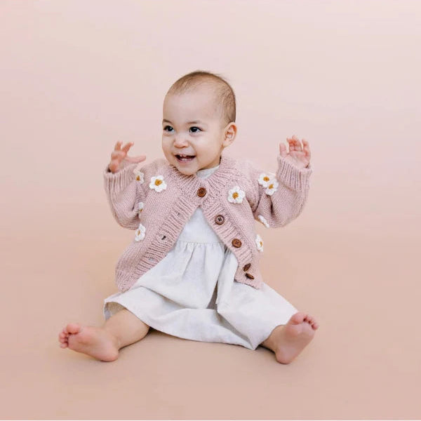 Baby wearing a pink cardigan with daisy buttons on a pink background