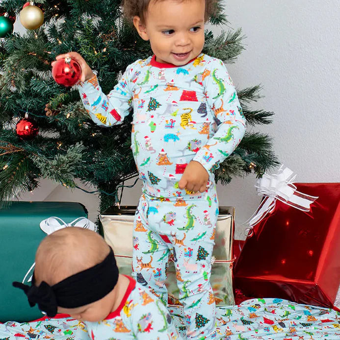 Two children in matching pajamas standing in front of a Christmas tree with presents.