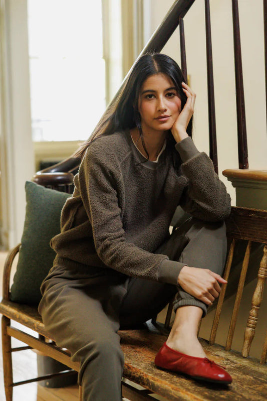 Woman wearing the Ziggy Fleece Long Sleeve crew sweatshirt in dark olive with olive colored pants and red flats 