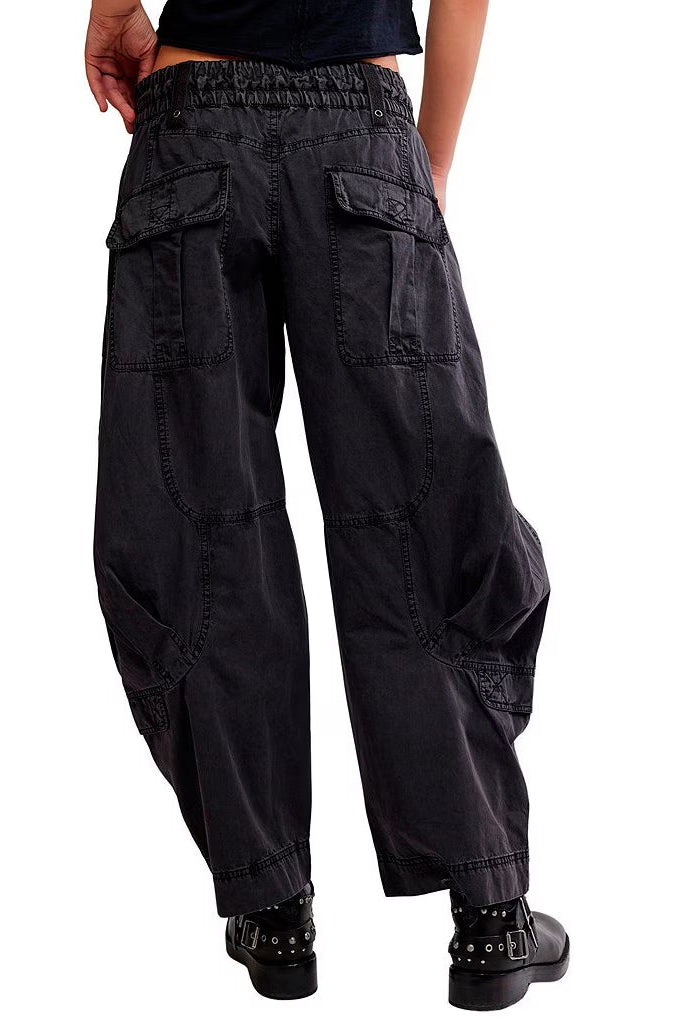 Black sand colored cargo pants with an elastic waistband, shown from the back on a model wearing black studded boots against a white background.