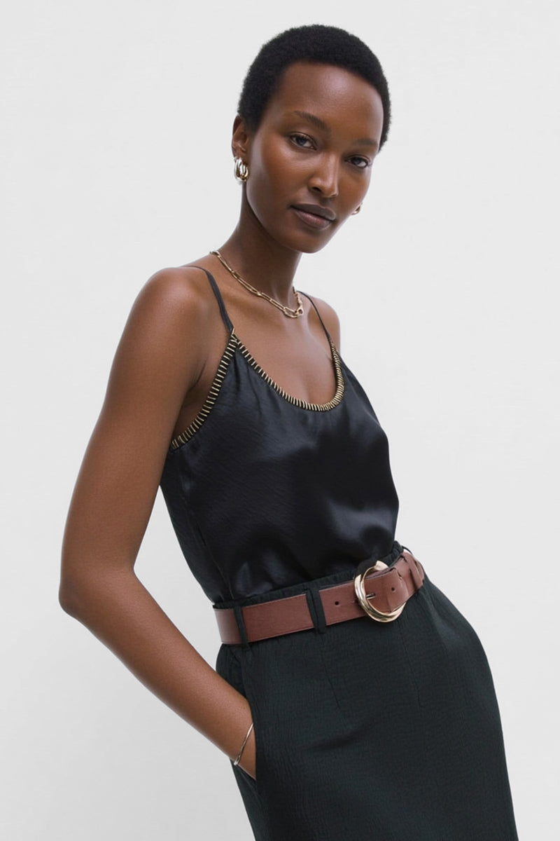 Woman wearing a black satin whipstitch top and brown belt against a white background