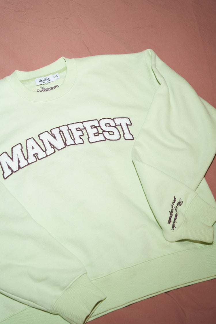Sage crewneck sweatshirt detail with MANIFEST logo graphic and small sleeve text