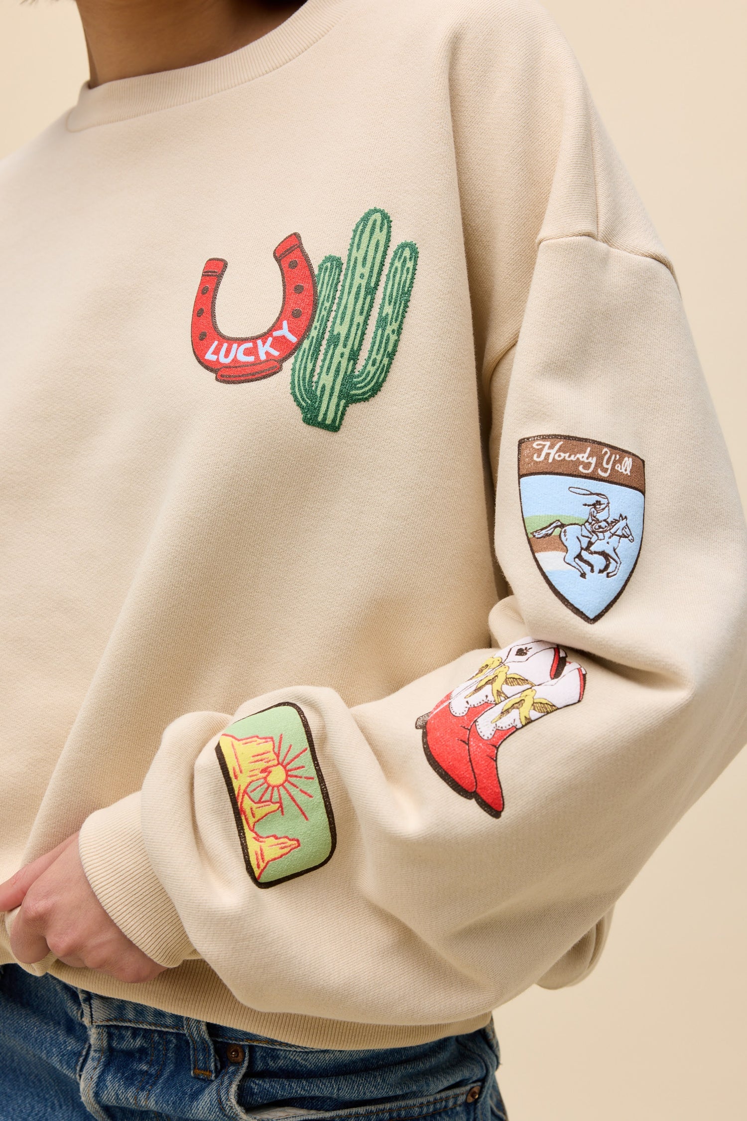 Sand sweatshirt with Lucky horseshoe, cactus patch, and shield graphic on sleeve cuff