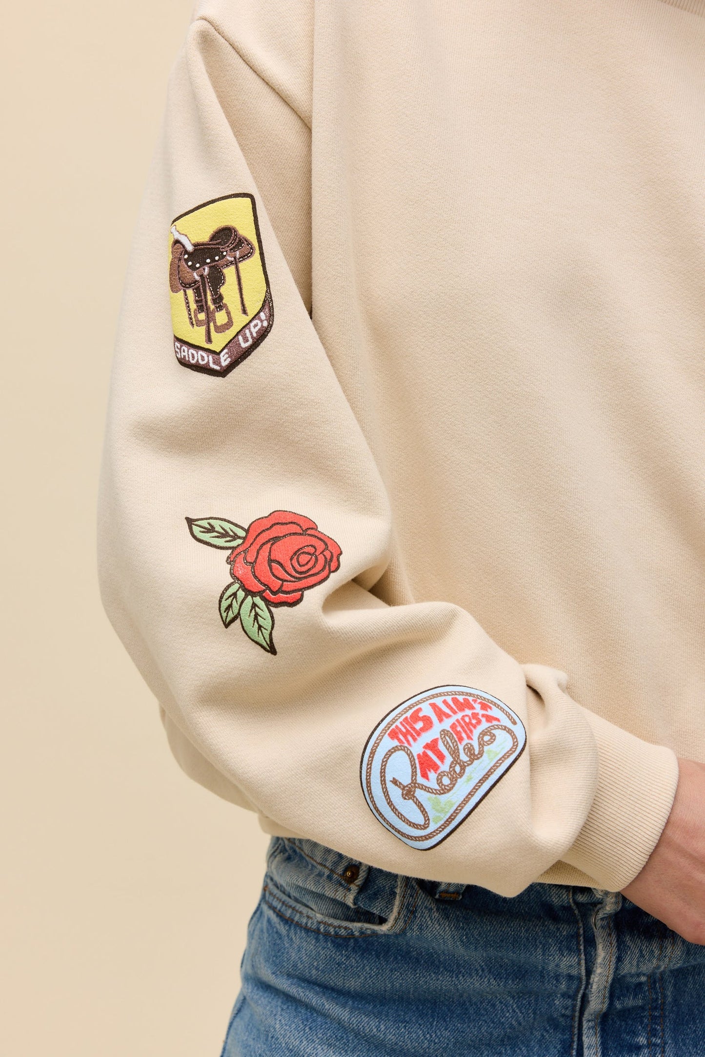 Sand sweatshirt sleeve with saddle patch, rose patch, and circular graphic on cuff