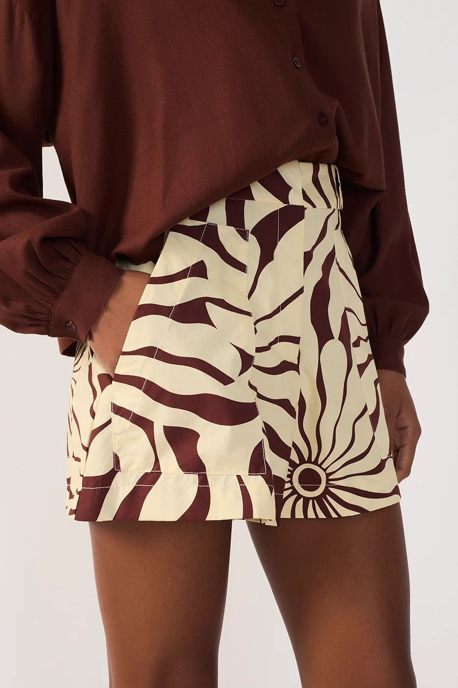 Person wearing a brown shirt and brown and beige alvorecer print shorts on a plain background