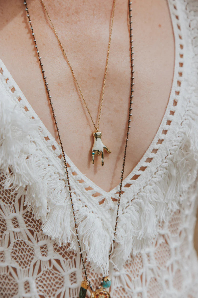 Gold layered necklace with hand charm pendant, green gem accents