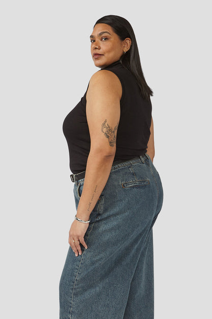 Denim trousers detail view, mid-rise waist and patch pockets on dark blue wash denim