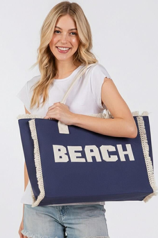 Denim blue tote bag with cream fringe trim and bold BEACH lettering