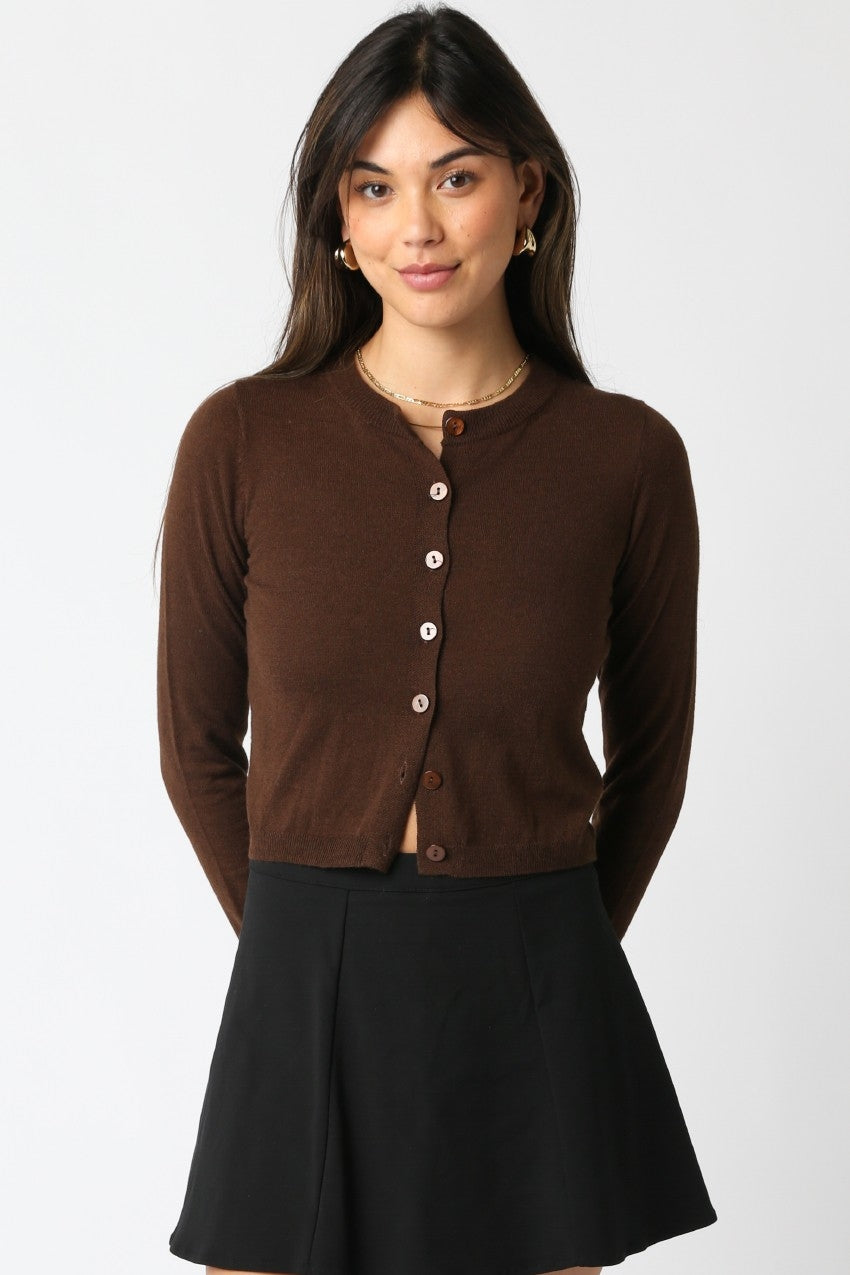 Woman wearing a brown button front cardigan over a black dress on a white background