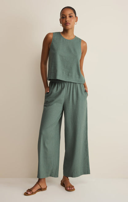 Woman wearing a green sleeveless top and wide-leg pants on a beige background