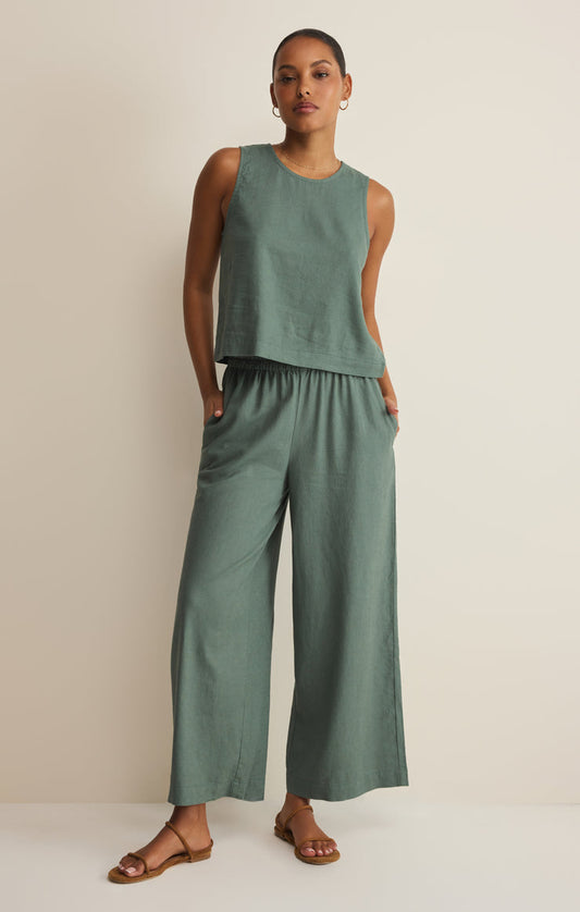 Woman wearing a green sleeveless top and wide-leg pants on a beige background