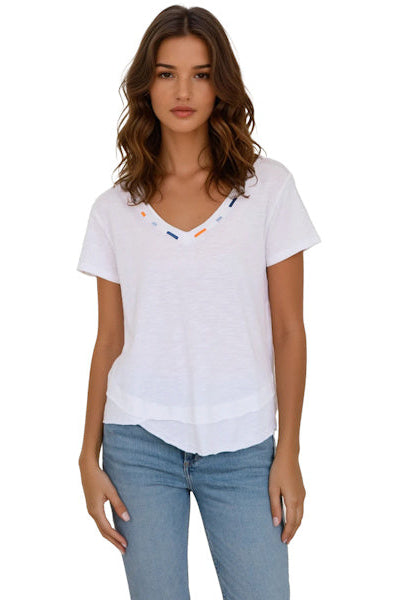 Woman wearing a white blouse with colorful accents and light blue jeans on a white background