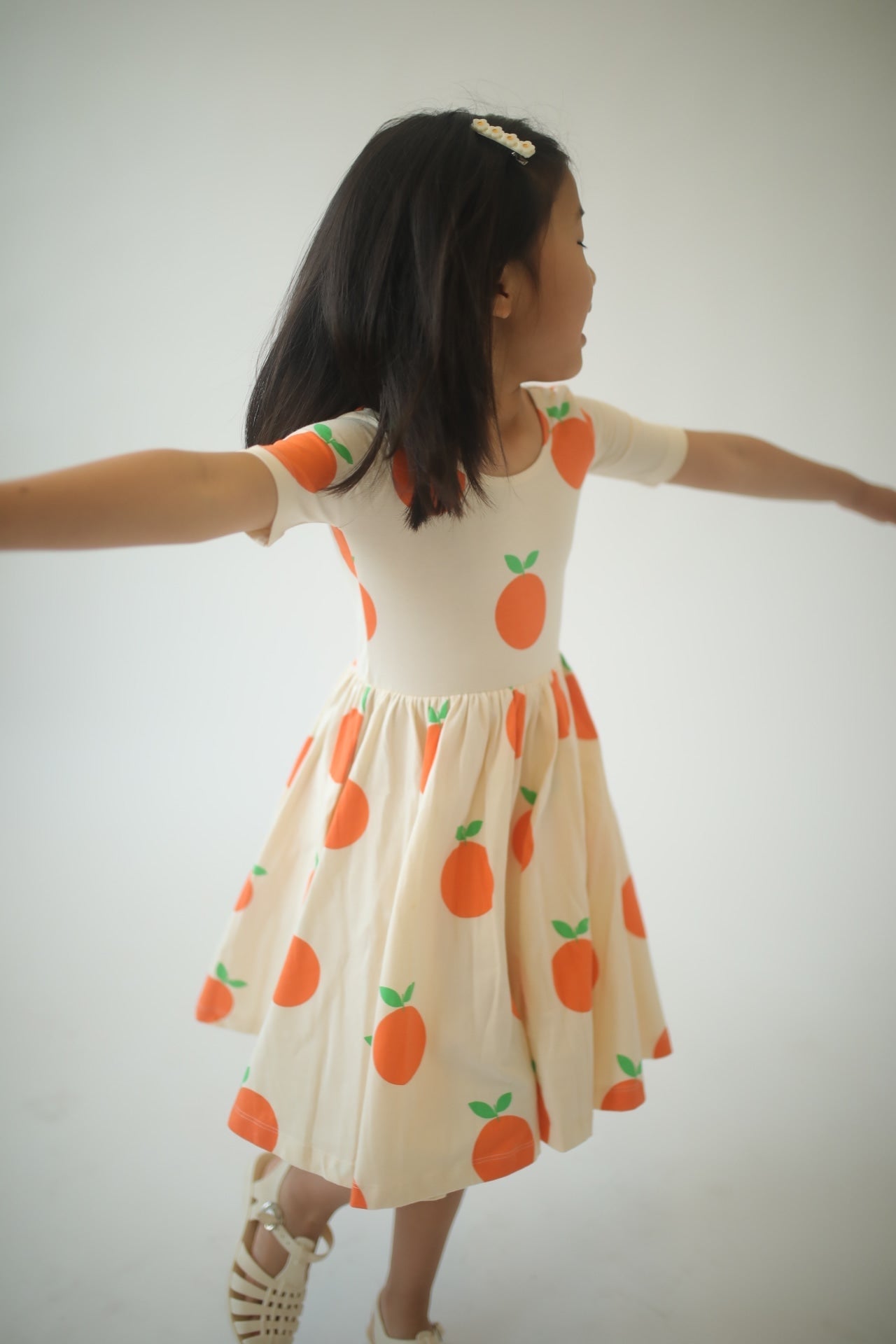 Girls orange fruit print twirl dress, back view with bows in hair