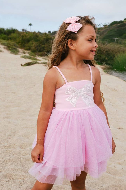 Young girl in a pink dress standing on a sandy beach with greenery in the background
