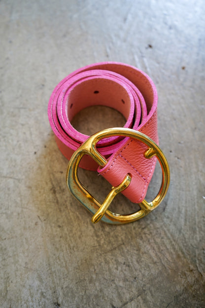 Pink belt with a gold buckle on a textured surface